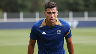 A determined, sweating 28-year-old Auxerre midfielder with a strong build, wearing a plain blue and amber training top...