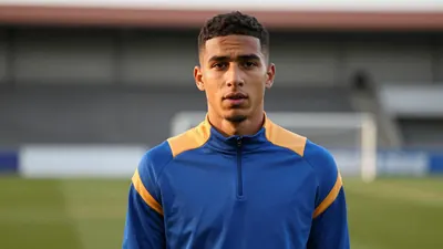 A young, athletic Auxerre forward, 22, with short dark hair and determined eyes, wears a plain blue and amber training...