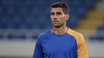 Mid-30s male coach, thoughtful expression, short dark hair, slight stubble, waist-up portrait, wearing a plain, unmarked...
