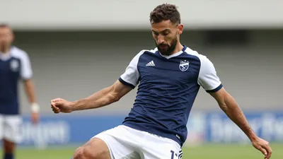 A tight action crop of a 30-year-old centre-back with a rugged build, wearing a navy blue jersey with white sleeves and a...