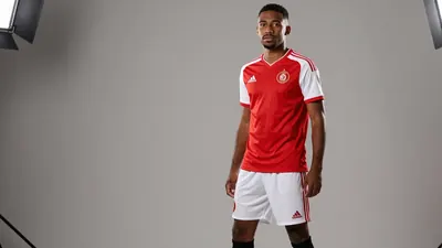 A photorealistic image of an anonymous Auxerre player in a red jersey with white sleeves, wearing a white pair of shorts...