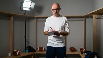 A 35-40 year old, athletic, balding, bespectacled man in his coaching kit, with a 3/4 length sleeve, a white shirt, and a...