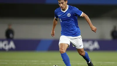 A 22-year-old midfielder, wearing a blue jersey with white shorts and black boots, is shown in a tight action crop, with...
