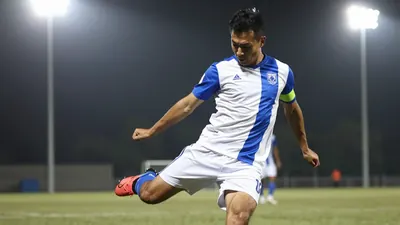 A 30-year-old male football player, wearing a blue and white jersey, taking a penalty kick with a determined expression