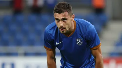Mid-30s Auxerre midfielder, athletic build, intense gaze, waist-up in a plain blue shirt with amber sleeves, smooth...