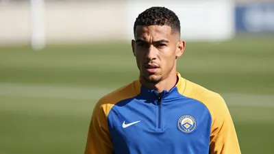 A determined 28-year-old Auxerre midfielder, with a strong build and focused expression, wears a plain blue and amber...