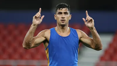 Mid-30s muscular forward, waist-up, intense gaze, short dark hair, slight stubble, wearing an unmarked training top split...