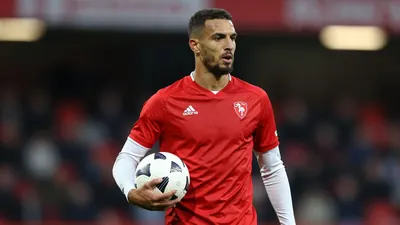 A photorealistic image of an anonymous Auxerre player in a red jersey with white sleeves, holding a white ball, with a...