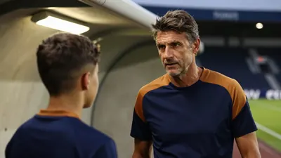 A 35-year-old male coach with a rugged build, standing in the tunnel of Stade de l'Abbé Deschamps, gazing intensely at a...